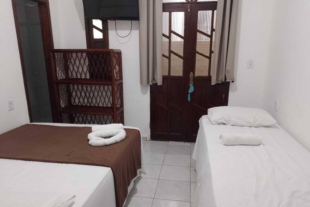 Une chambre d’hôtel avec deux lits, une cloison en bois et une porte avec un rideau.