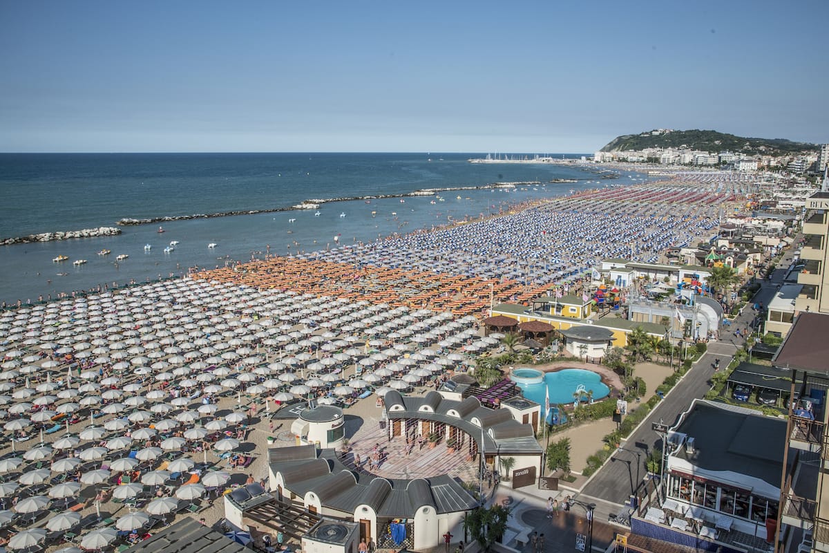 Een strand met veel parasols en mensen.