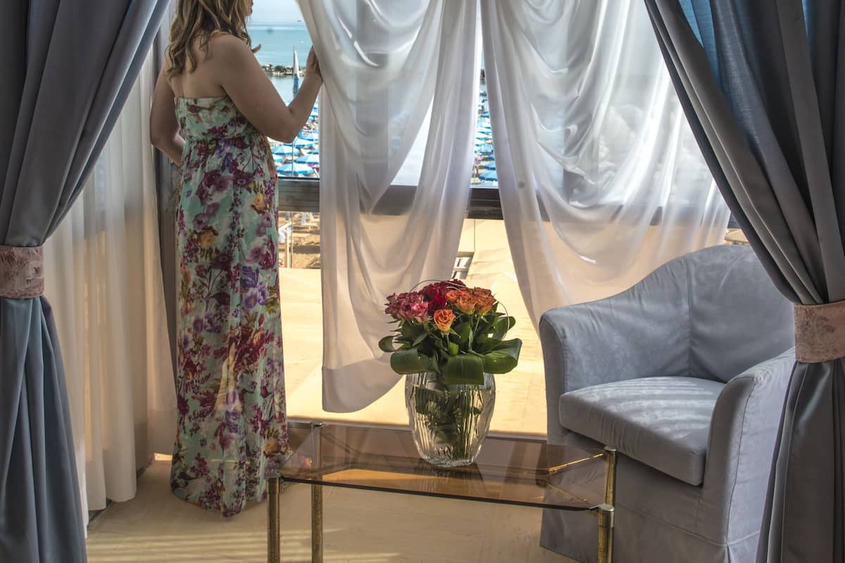 Een kamer met uitzicht op het strand, een stoel, een tafel en een vaas met bloemen.