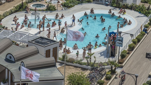 Une grande piscine extérieure entourée de nombreux parasols et de chaises longues, avec une vue sur la plage et l’océan en arrière-plan.