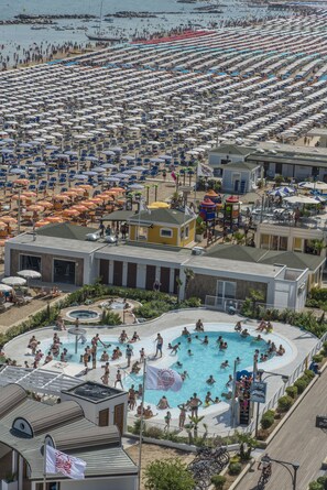 A large outdoor swimming pool surrounded by numerous beach umbrellas and lounge chairs, with a view of the beach and ocean in the background. - Hotel Baia Marina (Cattolica)