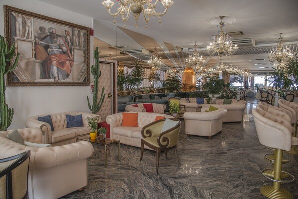 A spacious lobby with plush seating, a large mural, and ornate chandeliers. - Hotel Baia Marina (Cattolica)