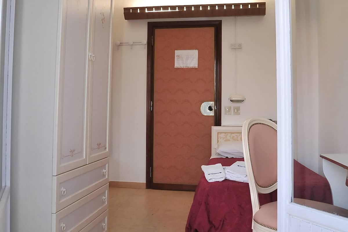 Een hotelkamer met een kledingkast, een bed met een rode sprei, een stoel en een klein tafeltje.