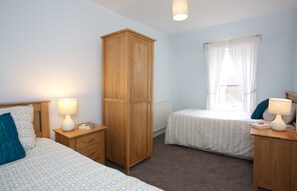 A bedroom with two beds, a wardrobe, and a window with curtains. - Avonlea (Crieff)