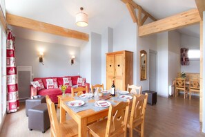 A dining area with a wooden table set for four, a red sofa with heart-patterned cushions, and a wooden cabinet. - Alpine Stay Near Slopes (Les Deux Alpes)