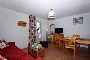 A living room with a red sofa, a wooden dining table, a TV, and a mirror. - Alpine Stay Near Slopes (Les Deux Alpes)