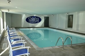 An indoor swimming pool with blue chairs lined up on one side and a sign reading 'Odaly's Vacances' on the wall.