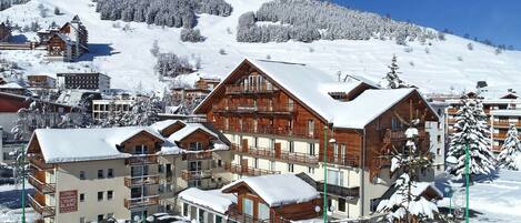 Un resort cubierto de nieve con edificios de madera, una pista de esquí al fondo y automóviles estacionados.
