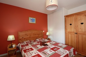 A bedroom with a wooden bed, red walls, a quilt, two bedside lamps, and a wardrobe with heart-shaped cutouts. - Versatile Apartments in French Alps (Les Deux Alpes)