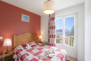 A bedroom with a wooden bed, two bedside lamps, a quilt, a stuffed toy, and a view of mountains through a window.
