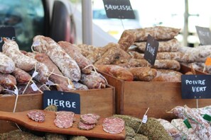 Verschiedene Wurstsorten, luftgetrocknet und in Holzkisten präsentiert, mit Schildern, die Sorten wie 'Herbe', 'Saucisse', 'Fume' und 'Poivre Vert' bezeichnen.