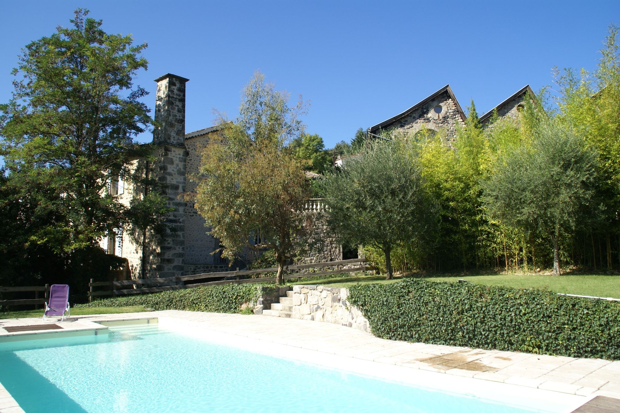 A swimming pool with a stone staircase leading to a building, surrounded by greenery and trees.
