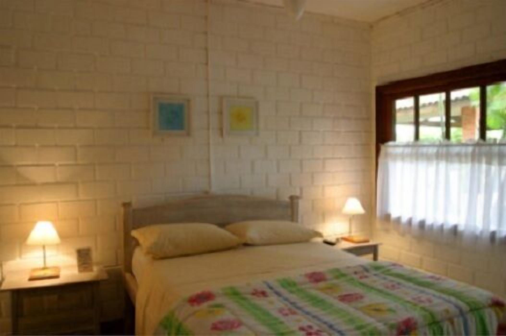 Un dormitorio con pared de ladrillo, cama con ropa de cama floral, dos lámparas de noche y una ventana con cortinas.