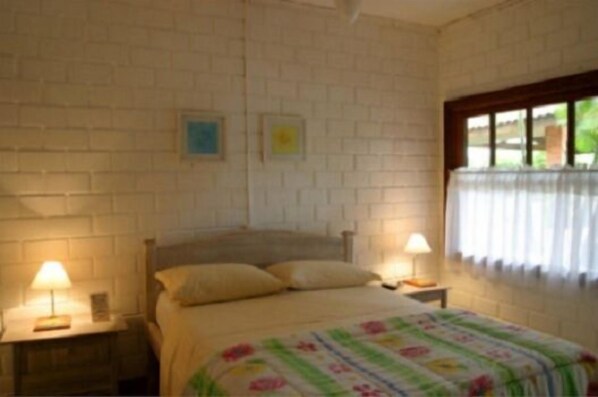 Un dormitorio con pared de ladrillo, cama con ropa de cama floral, dos lámparas de noche y una ventana con cortinas.