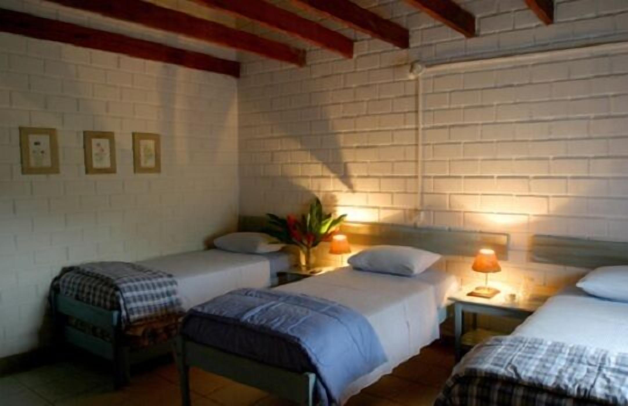 A room with two single beds, a brick wall, and a wooden ceiling.