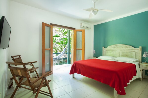 A bedroom with a bed, a nightstand, a chair, a TV, and a door leading to a balcony. - Pousada do Rosa (São Sebastião)