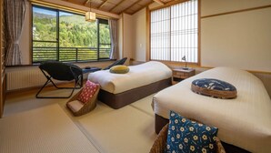 A bedroom with two beds, a chair, a nightstand, and a view of a forest through large windows. - Kinosato (Yamagata)