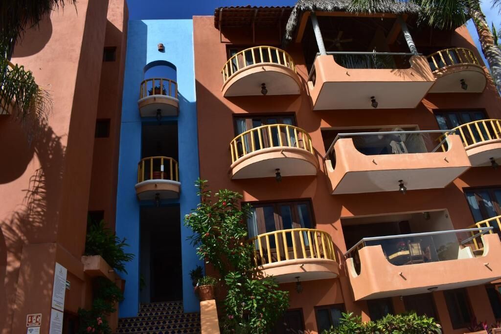 A multi-story hotel with balconies, a blue facade, and potted plants.