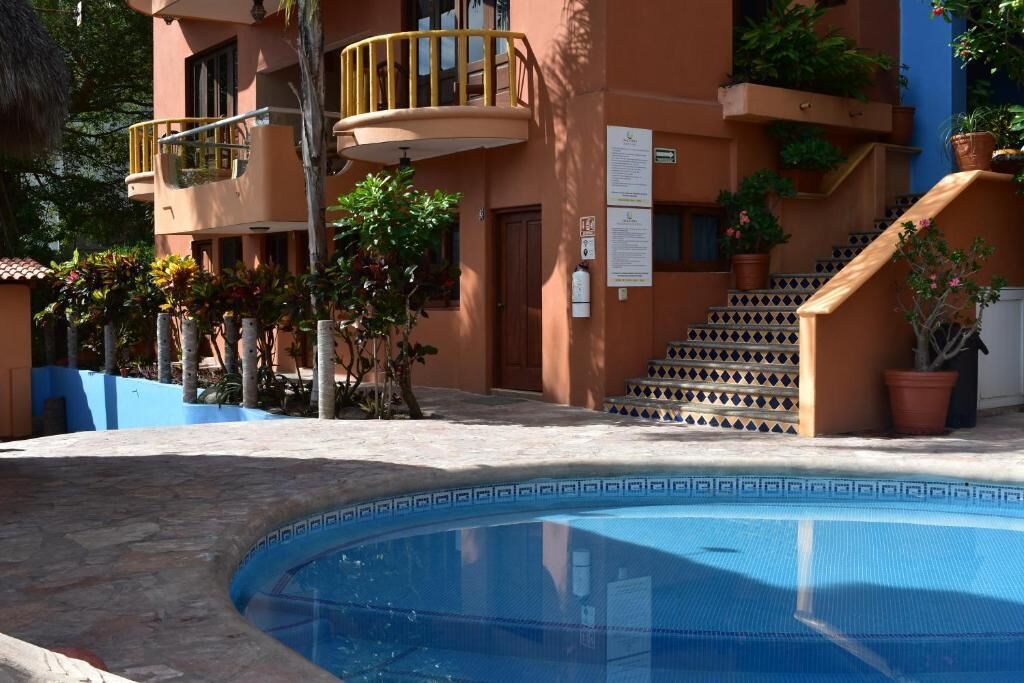 Un área de piscina con borde curvo, una escalera con baldosas estampadas y un edificio con balcones y plantas en macetas.