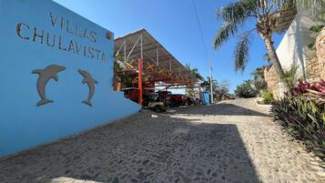 Señal de 'Villas Chulavista' con dos esculturas de delfines, un área de estacionamiento techada y un camino de arena que lleva a la entrada.