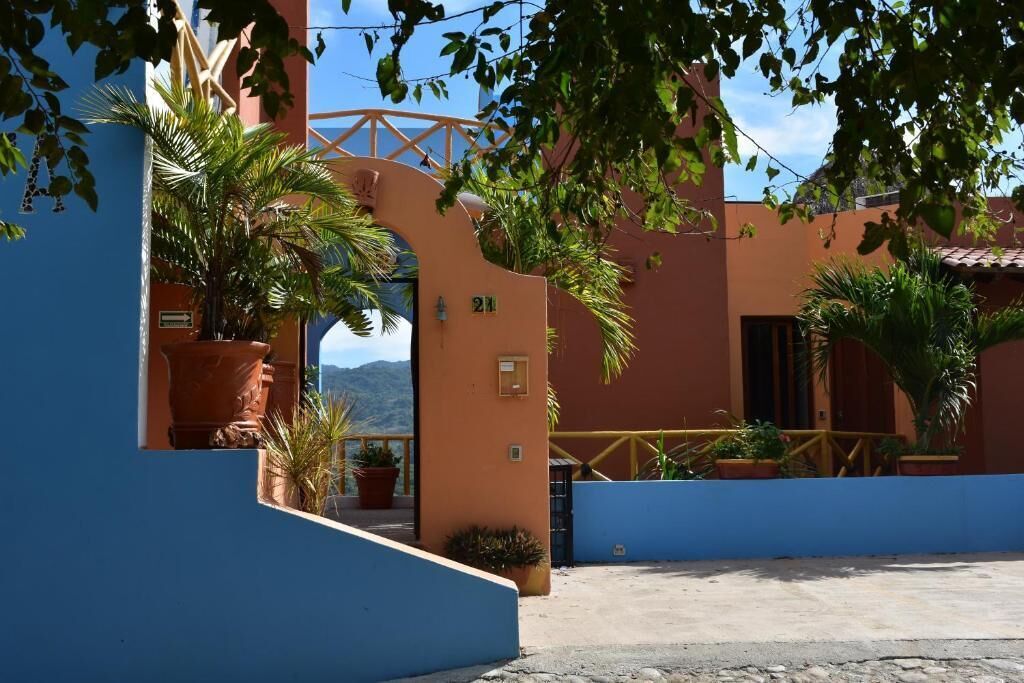 Un bâtiment à la façade bleue, orné de pots en terre cuite et doté d’un balcon avec une balustrade en bois.