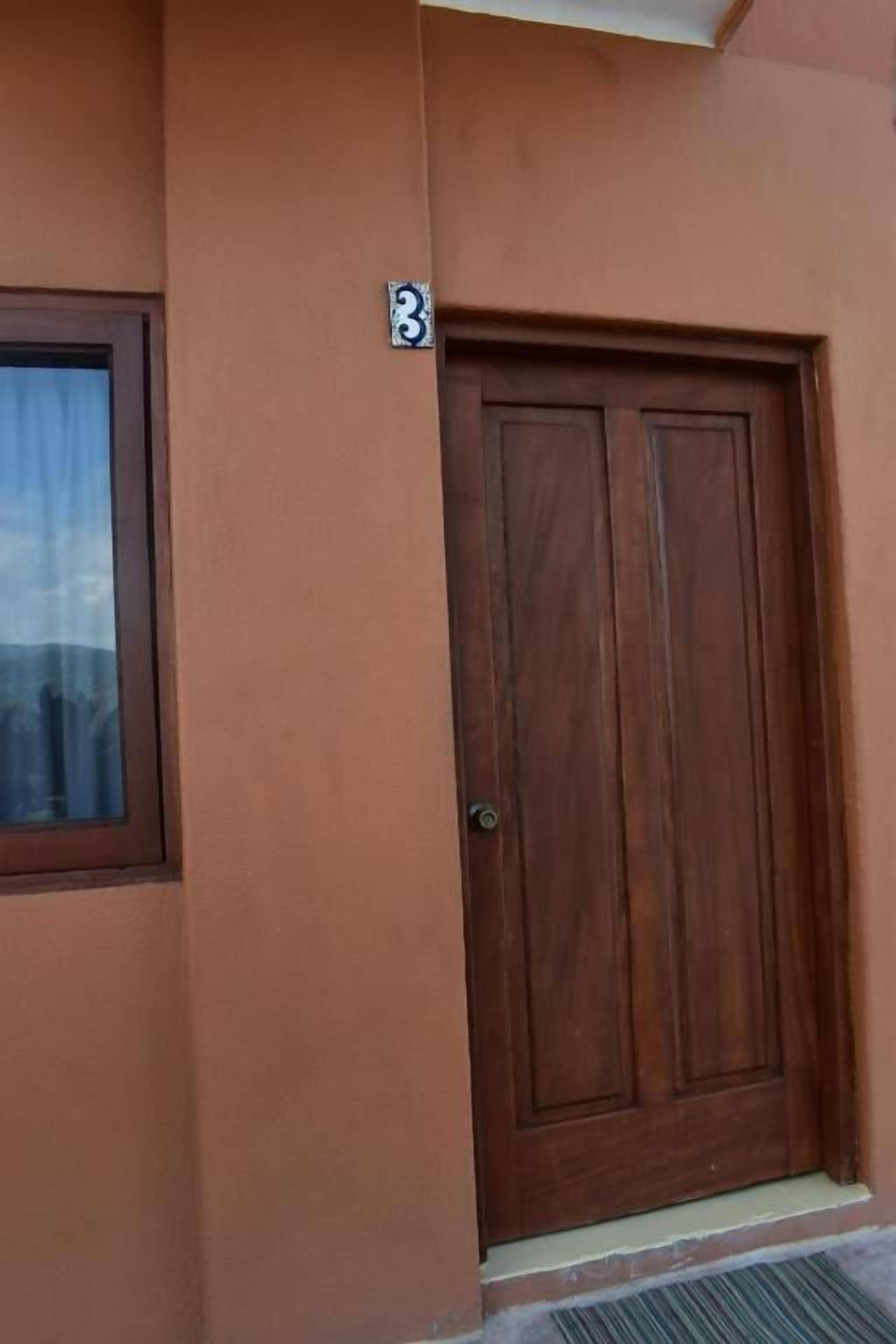 Una puerta marrón con un cartel con el número 3, indicando el número de habitación.