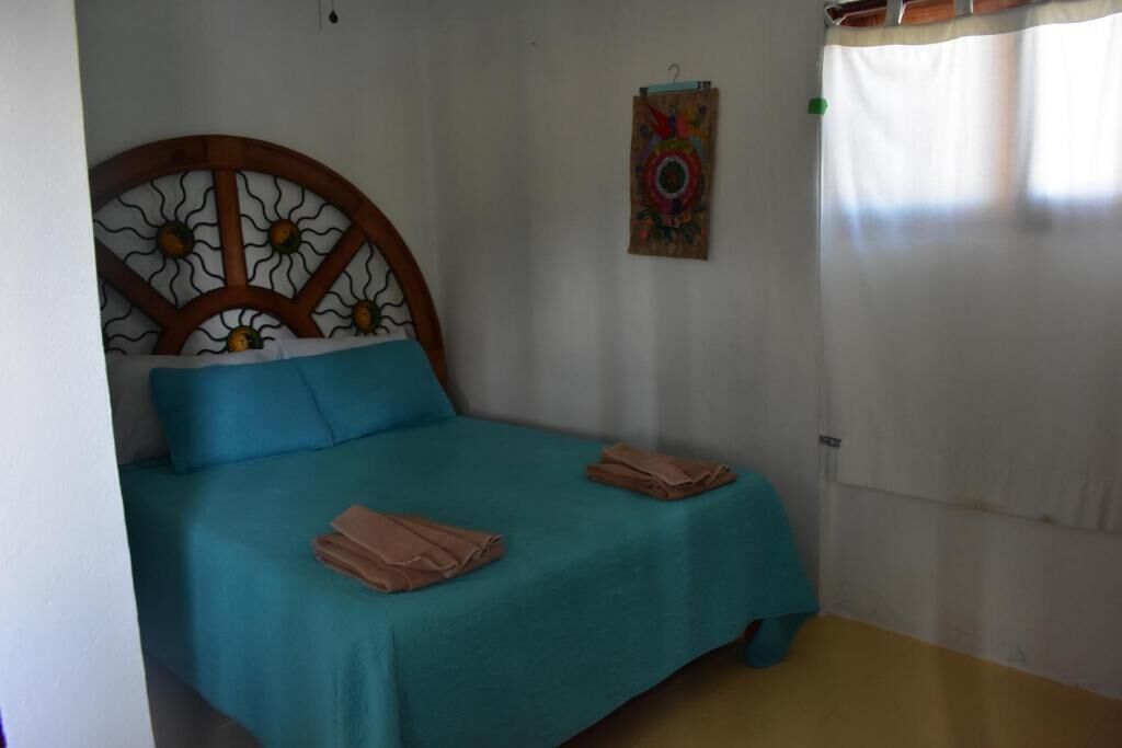 Ein Schlafzimmer mit Bett, einem an der Sonne erinnernden Kopfteil, einem farbenfrohen Kunstwerk an der Wand und einem Vorhang.