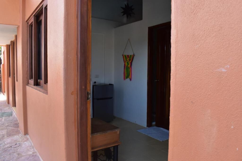 Un couloir étroit avec une porte en bois, une petite table et un réfrigérateur au fond.