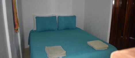 Ein kleiner, schlichter Raum mit einem Bett, zwei Kissen und zwei gefalteten Handtüchern.
