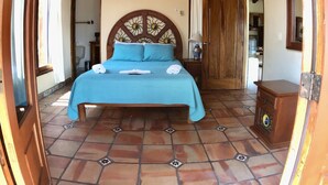 Une chambre à coucher avec un lit, un ventilateur de plafond, une tête de lit en bois et un plancher carrelé.