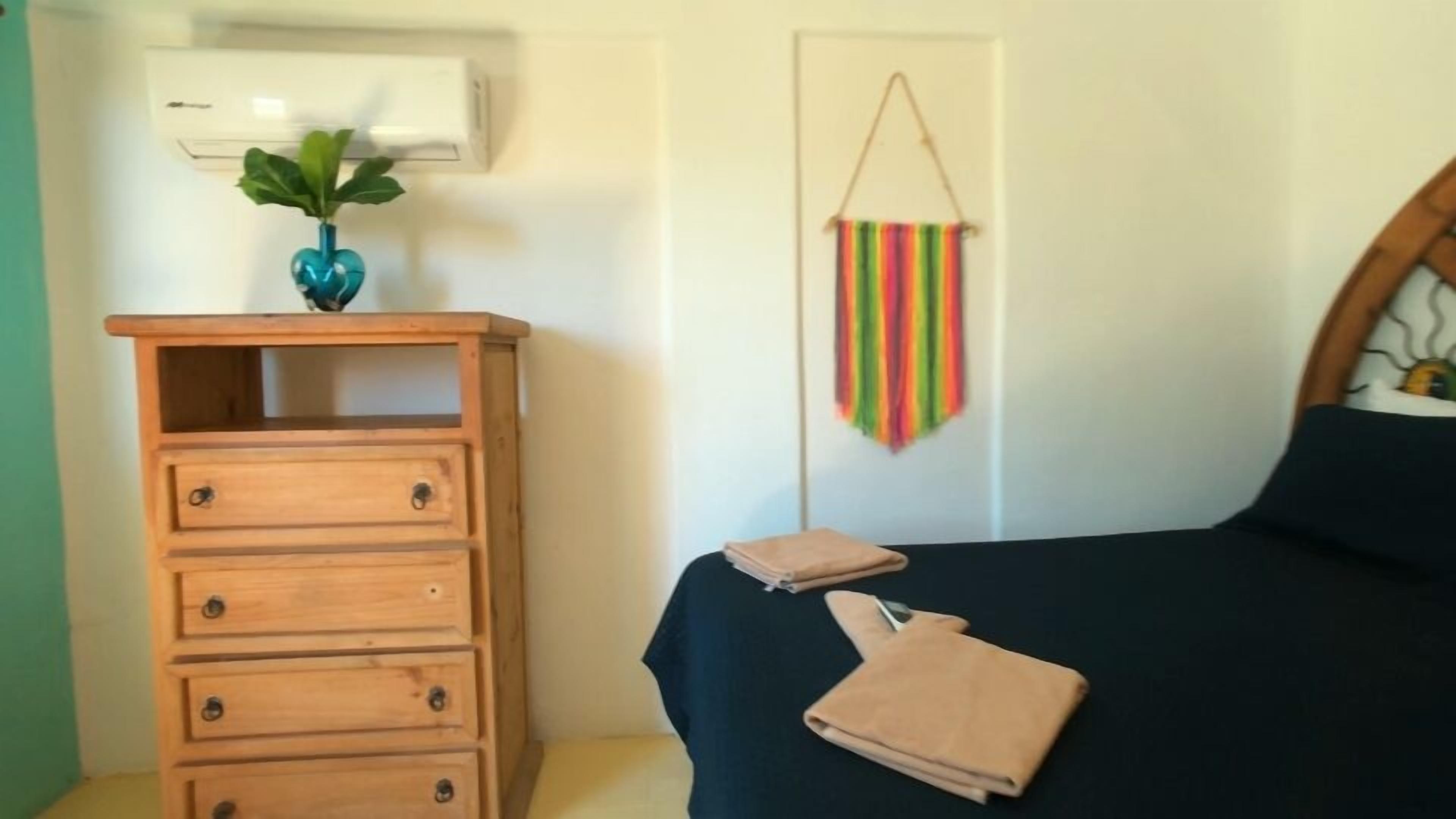 Un dormitorio con un aparador de madera, una cama con cubierta oscura y un adorno colgante.