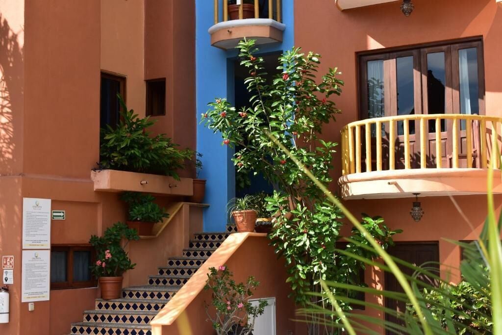 A multi-story building with a staircase leading to a balcony. There are potted plants on the balconies and steps.
