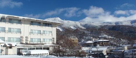 Un hotel de diseño arquitectónico moderno, con múltiples ventanas y unidades de aire acondicionado. El hotel está ubicado en una zona montañosa nevada, con edificios y árboles cubiertos de nieve a la vista.