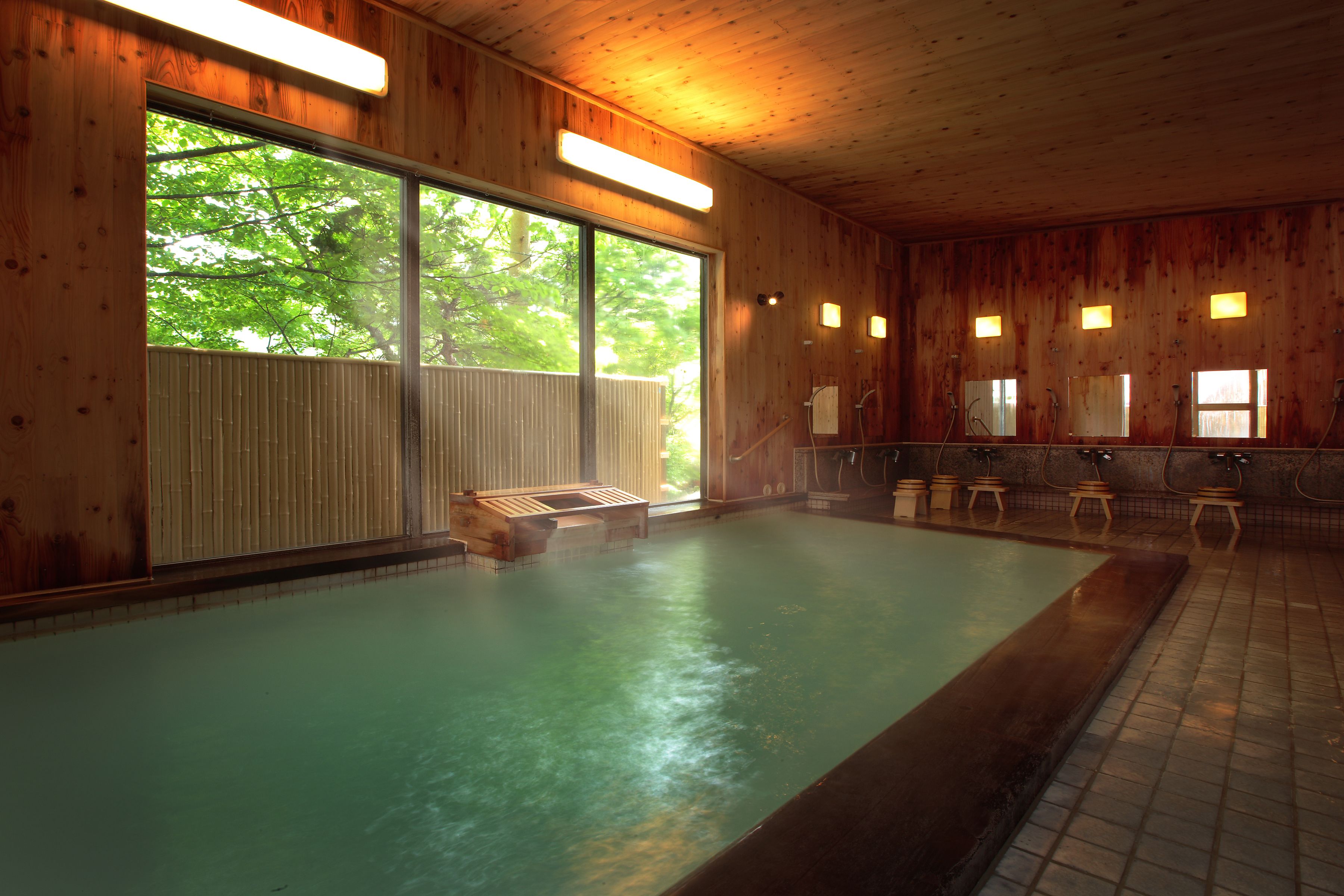 A wooden interior with a large indoor pool, benches, and a sauna area.