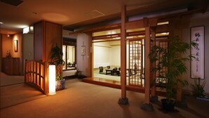 Un interior japonés tradicional con suelo de tatami, puertas correderas y una zona de recepción con mostrador y plantas.