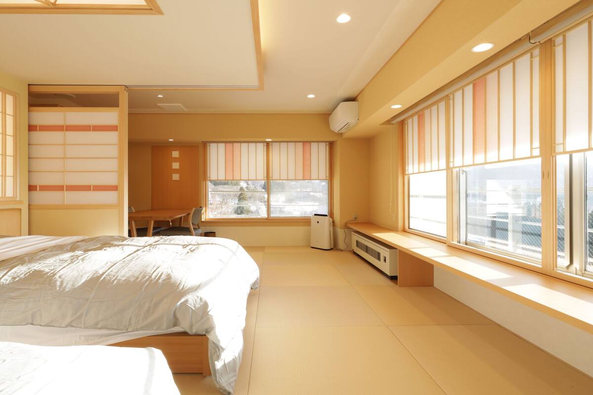 A bedroom with a bed, a desk, and a window with blinds.