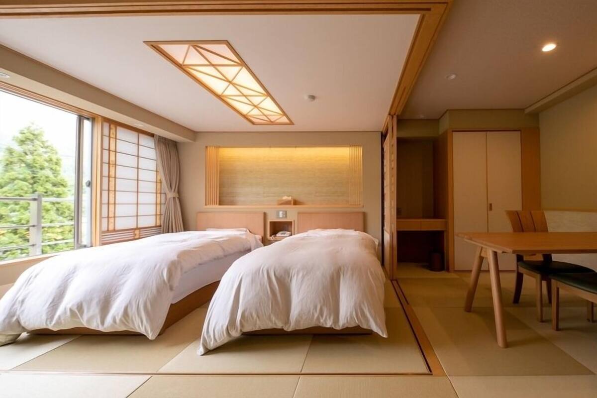 A hotel room with two beds, a dining table, and a view of the outdoors.