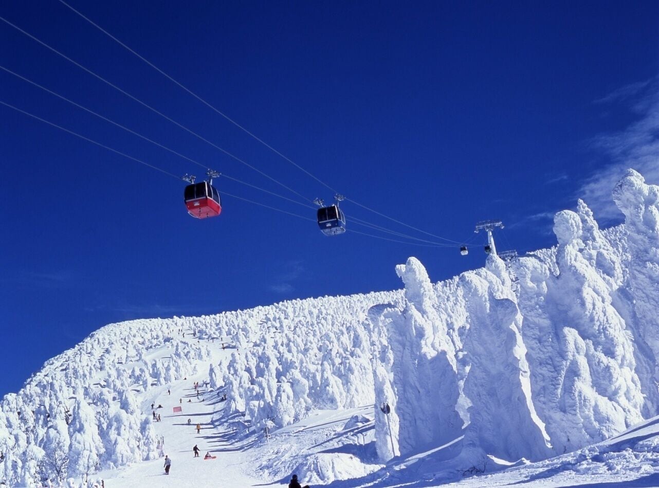A ski lift with cabins moving over a snowy mountain slope.