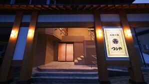 Entrada de un edificio tradicional japonés, con columnas de madera y un letrero iluminado.