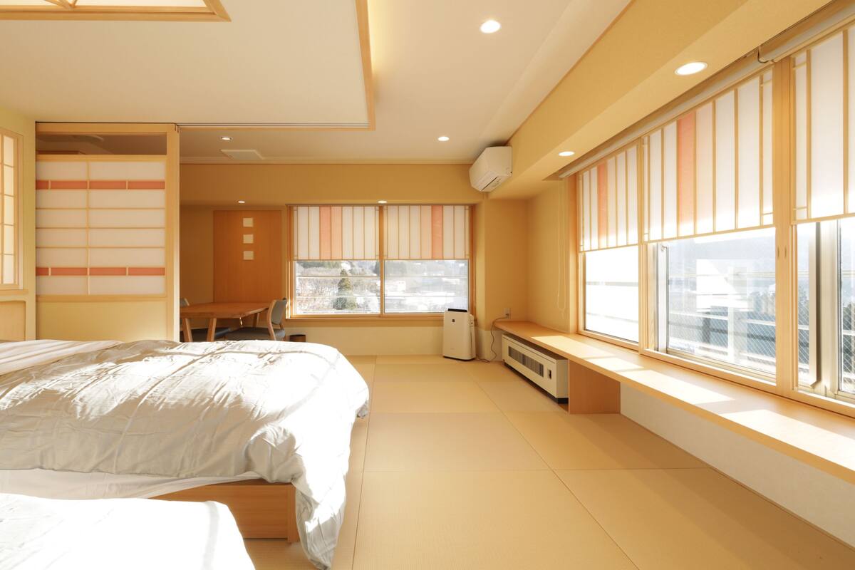A bedroom with a bed, a desk, and a window with blinds.