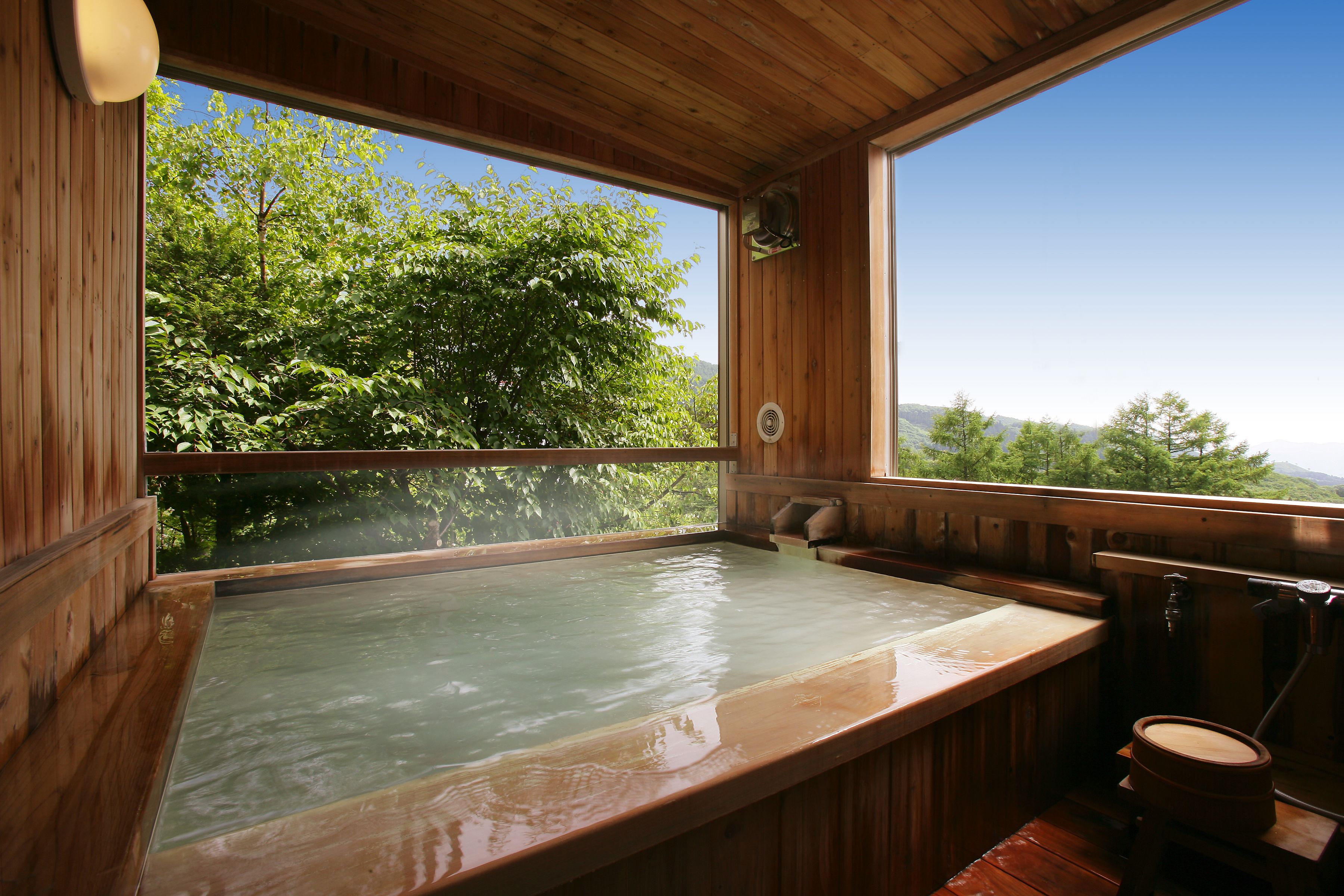 Un área de spa de madera con un jacuzzi, bancos de madera y vistas a árboles y montañas.