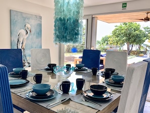 A dining area with a table set for four, featuring blue and white plates, bowls, and cups. There is a painting of a bird on the wall, and a hanging light fixture above the table. - Casa Iguana del Mar (San Andrés)