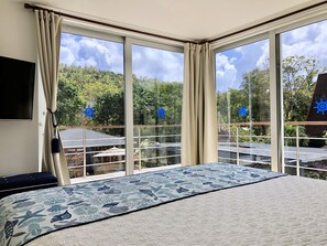 A bedroom with a large bed, a TV, and a view of a balcony with outdoor furniture and greenery. - Casa Iguana del Mar (San Andrés)