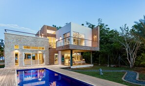 A modern two-story house with a pool, large windows, and a balcony.