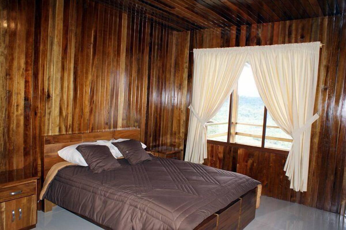 A wooden cabin room with a bed, curtains, and a window.