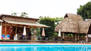 A pool area with a bar, thatched-roof structures, and outdoor seating. - Hosteria Farallon (Sevilla Don Bosco)