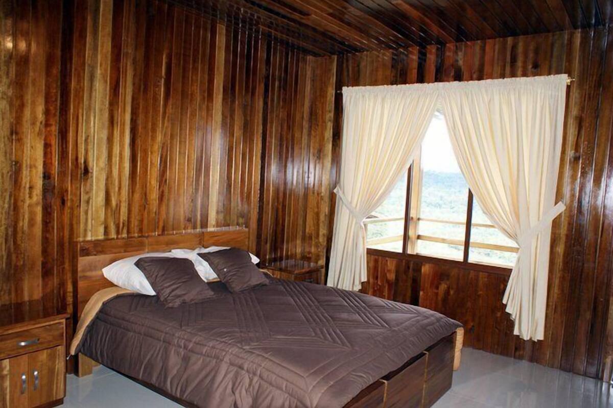 A wooden room with a bed, curtains, and a window.
