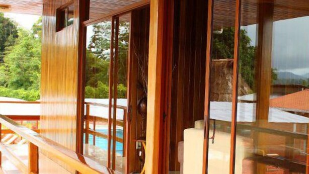 A wooden room with large windows, a view of a pool, and a mountain in the background. - Hosteria Farallon (Sevilla Don Bosco)