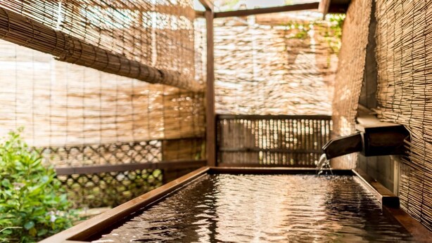 A hot spring area with a wooden bench and a water feature. - Hotel Yamakawa (Yonezawa)
