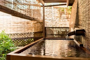 A hot spring area with a wooden bench and a water feature. - Hotel Yamakawa (Yonezawa)